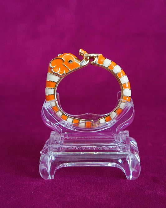Hinged orange and cream enamel bangle shaped like an elephant curling around the wrist