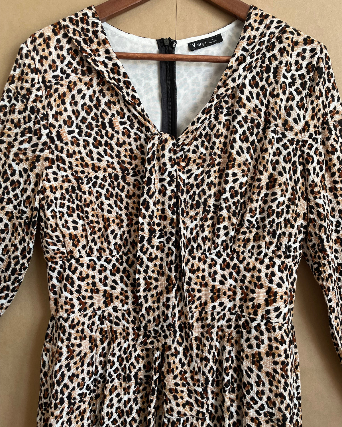 A Very J leopard print romper with a tie-neck V and bell sleeves, shown against a kraft background