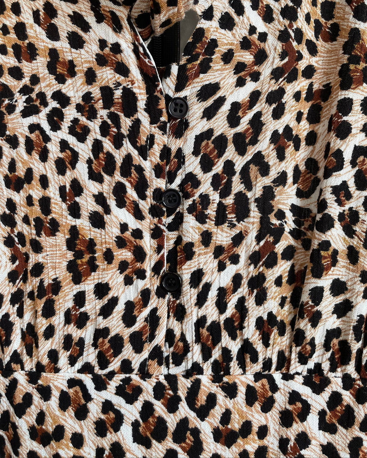 A Very J leopard print romper with a tie-neck V and bell sleeves, shown against a kraft background
