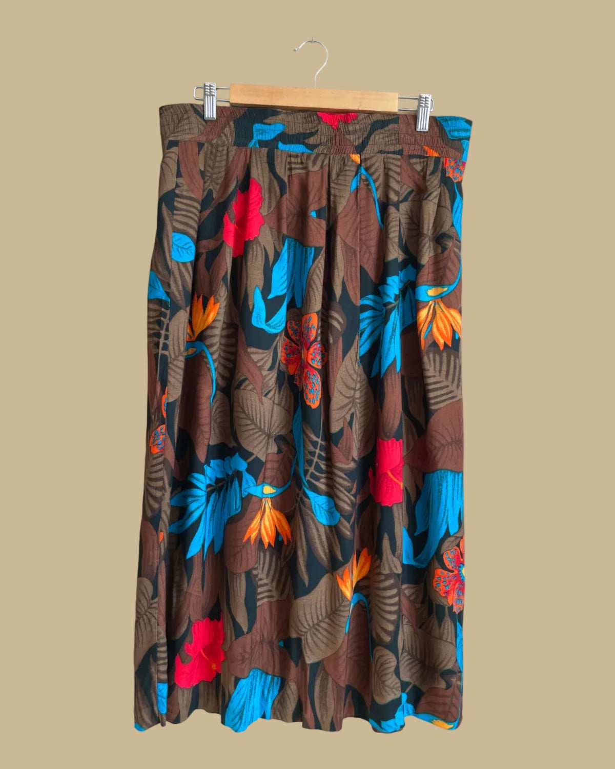A vintage tropical bird-of-paradise print pleated skirt in brown, black, teal, and orange tones, shown against a kraft background