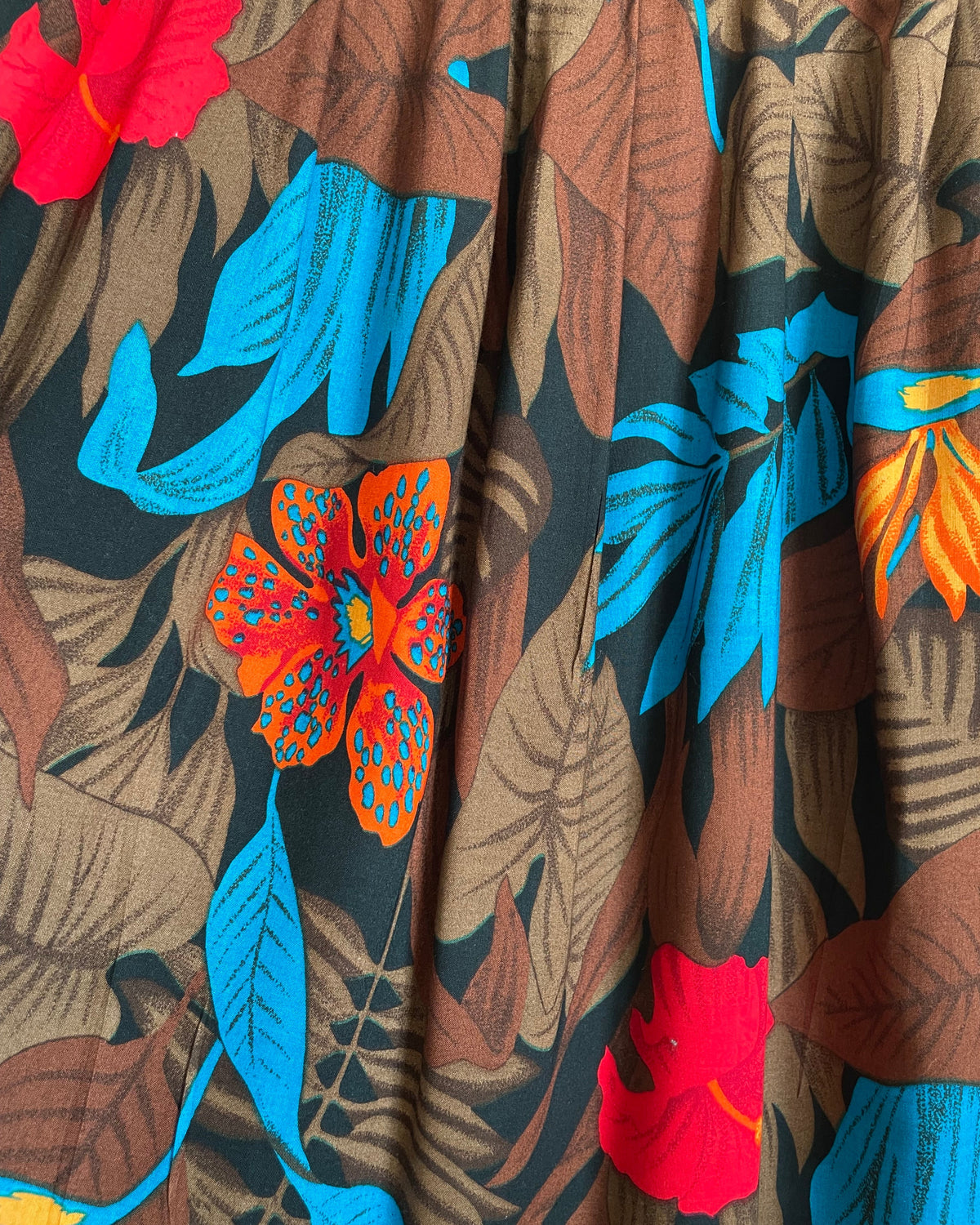 A vintage tropical bird-of-paradise print pleated skirt in brown, black, teal, and orange tones, shown against a kraft background