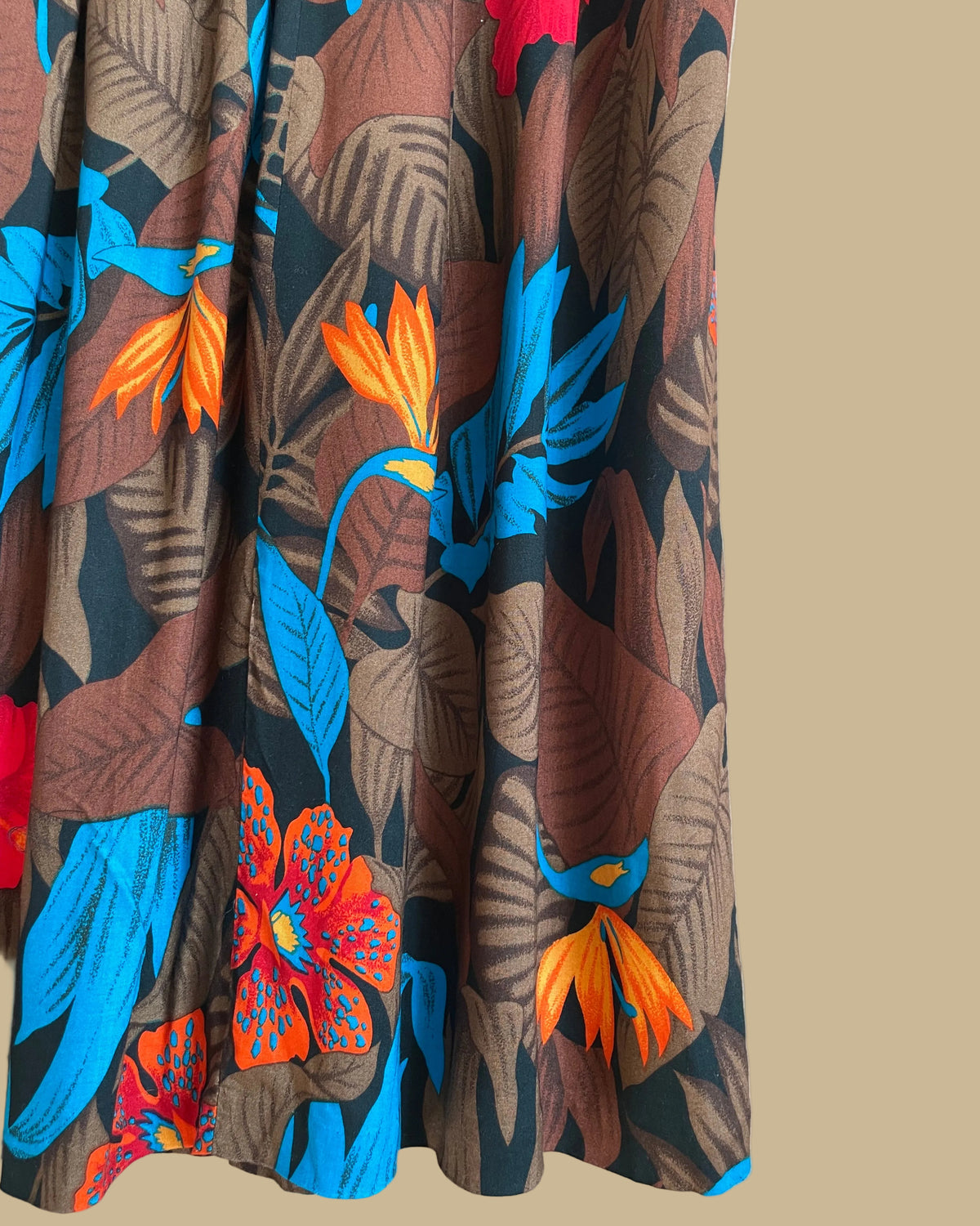 A vintage tropical bird-of-paradise print pleated skirt in brown, black, teal, and orange tones, shown against a kraft background