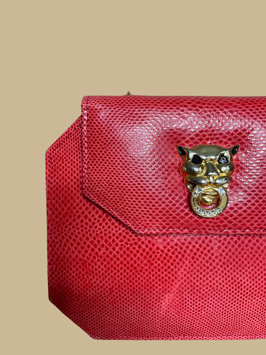 A small red textured snakeskin handbag with a gold-tone panther head clasp, shown on a neutral beige background with its matching chain strap