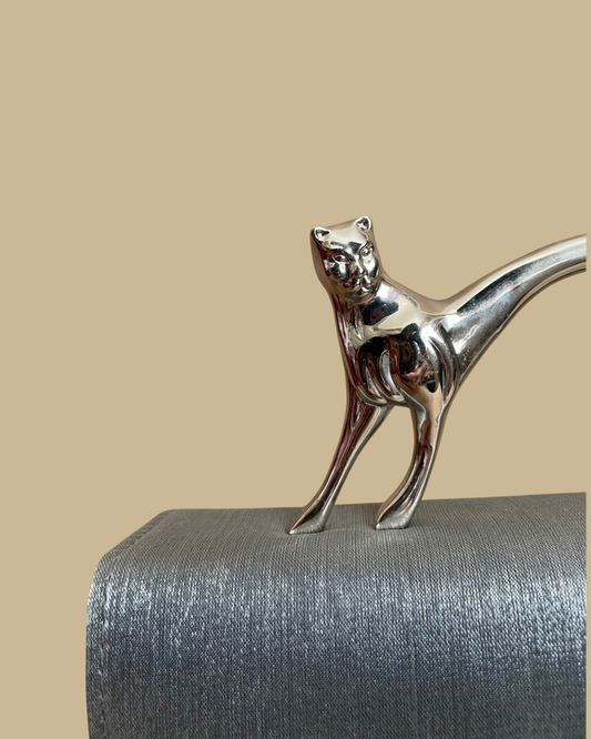 Pewter-silver metallic evening bag with a polished chrome feline handle across the flap