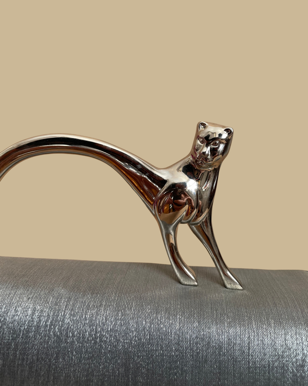 Pewter-silver metallic evening bag with a polished chrome feline handle across the flap