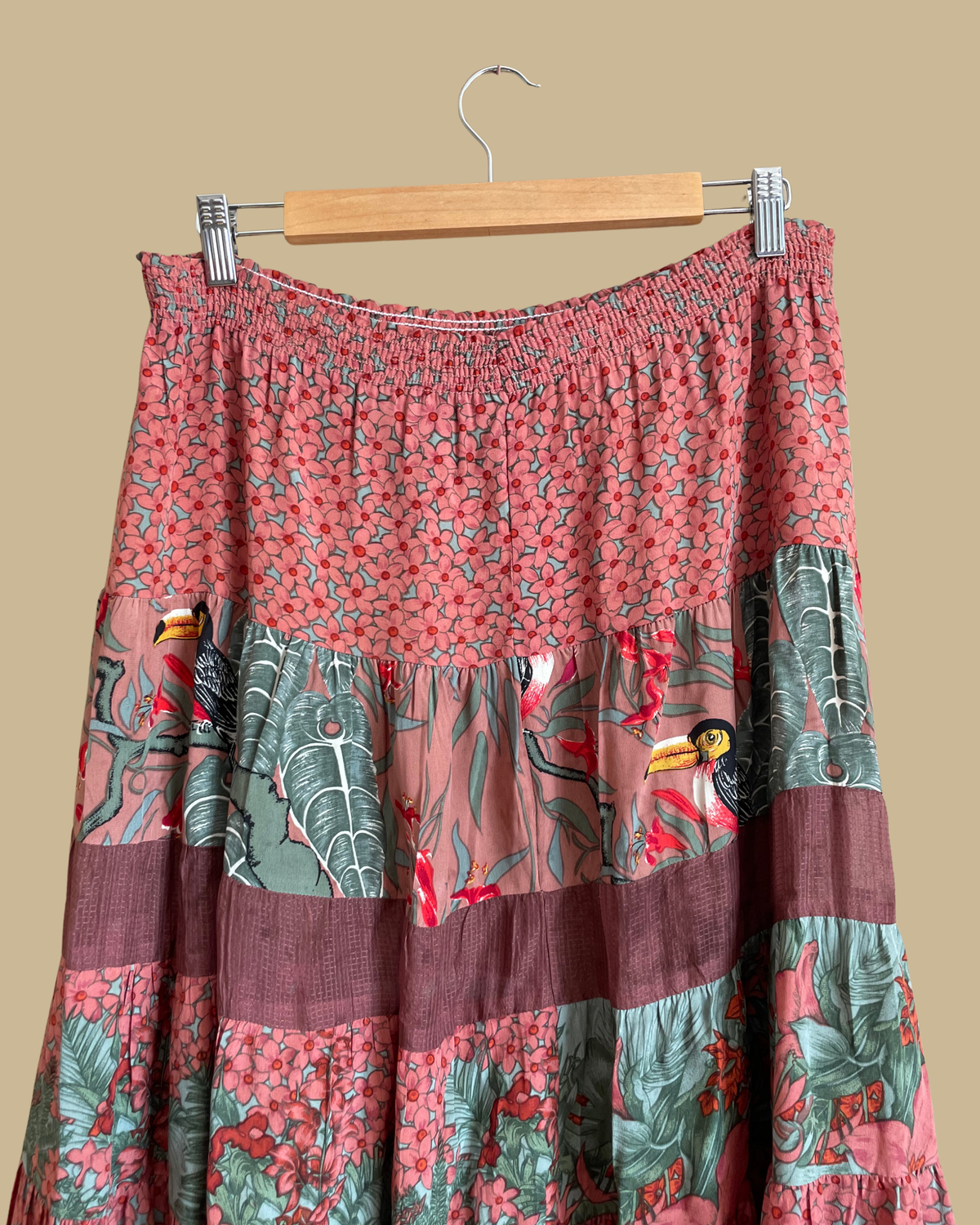 A vintage Carole Little tiered silk skirt with a tropical toucan and floral print in brown, teal, and orange tones, shown against a kraft background