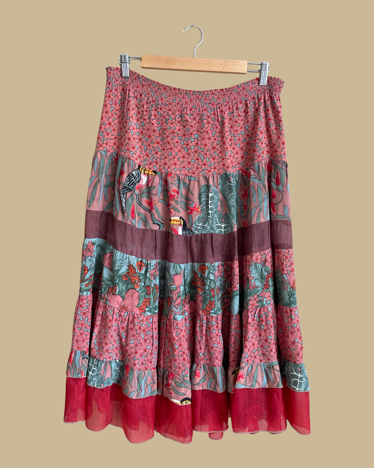A vintage Carole Little tiered silk skirt with a tropical toucan and floral print in brown, teal, and orange tones, shown against a kraft background