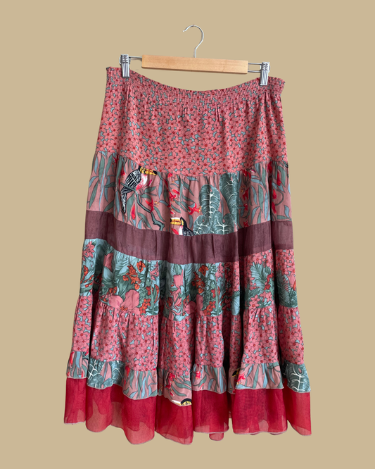 A vintage Carole Little tiered silk skirt with a tropical toucan and floral print in brown, teal, and orange tones, shown against a kraft background