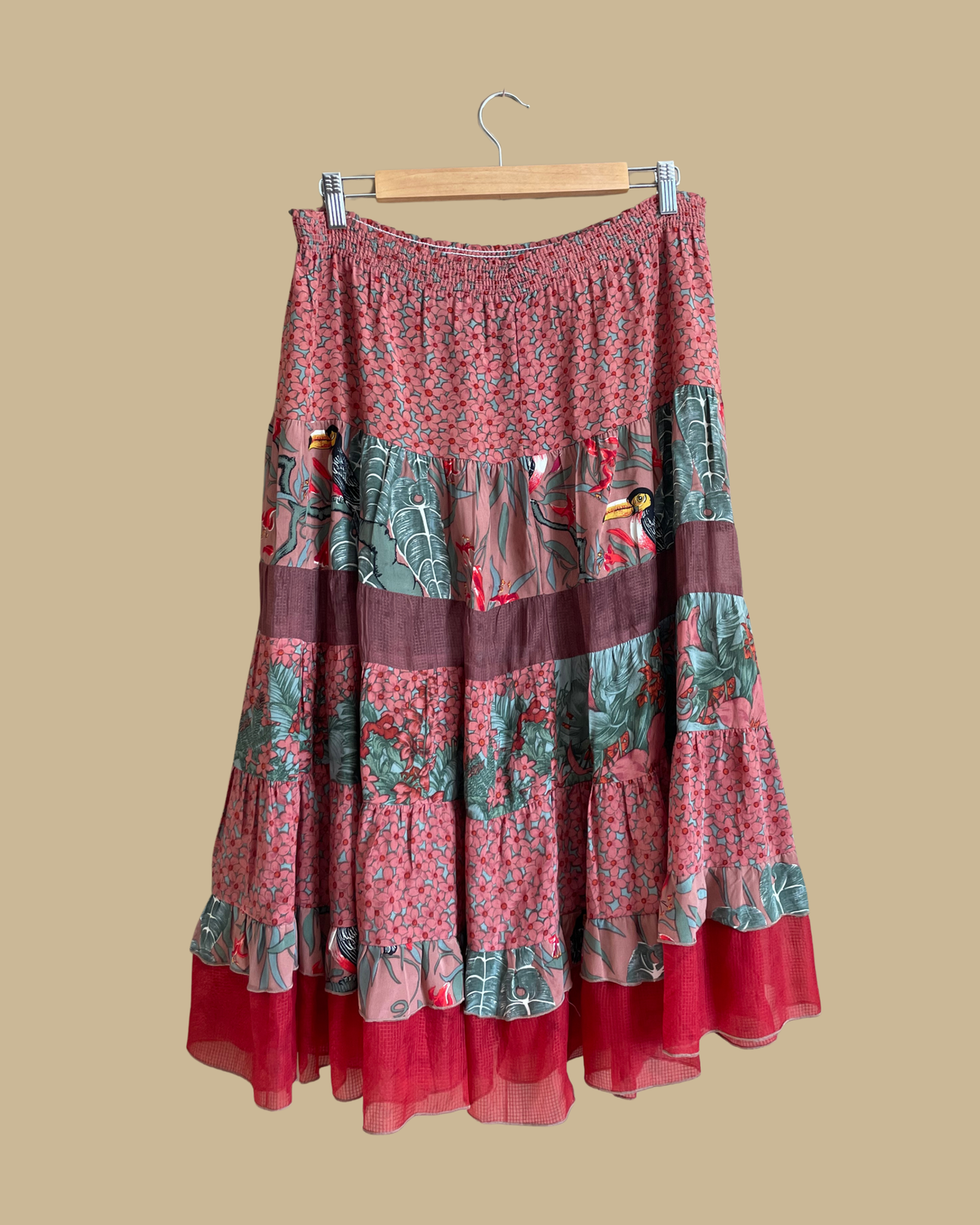 A vintage Carole Little tiered silk skirt with a tropical toucan and floral print in brown, teal, and orange tones, shown against a kraft background
