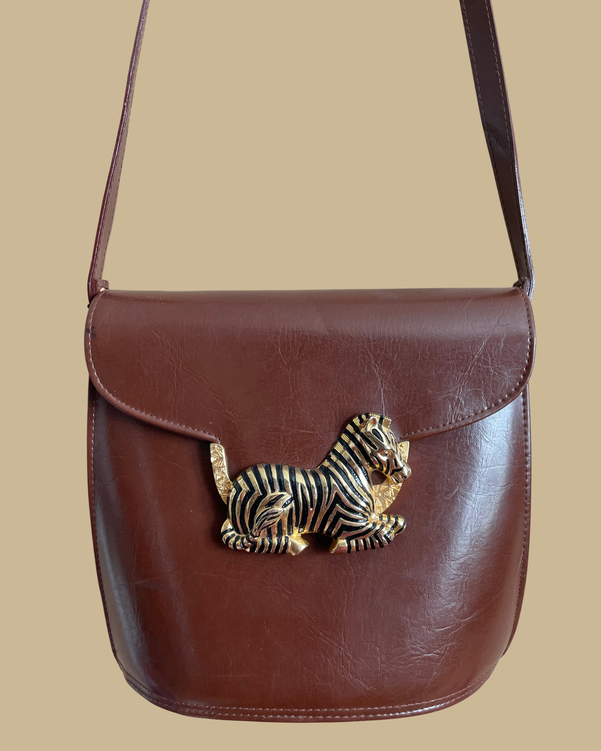 A vintage brown crossbody bag with a sculptural gold-tone and black enamel zebra clasp on the flap closure, shown against a kraft background