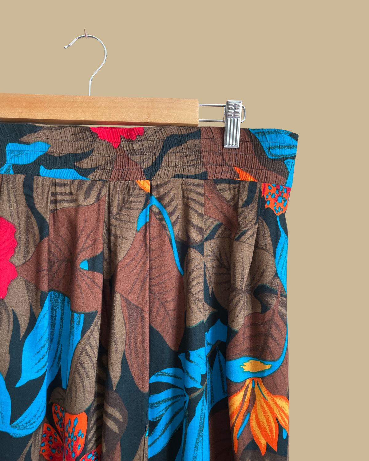 A vintage tropical bird-of-paradise print pleated skirt in brown, black, teal, and orange tones, shown against a kraft background
