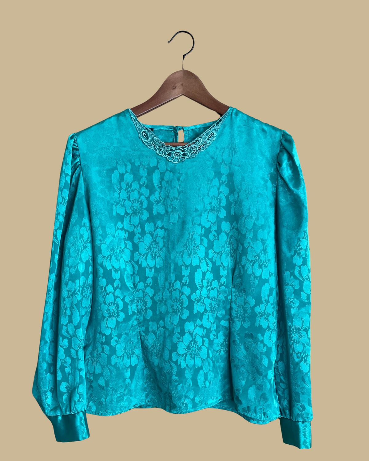 A vintage Ann Chabrol teal floral jacquard blouse on a hanger against a neutral beige background