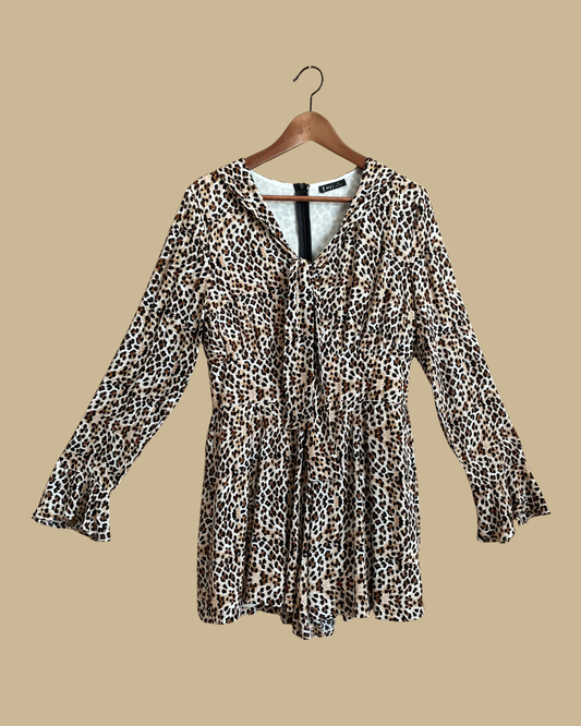 A Very J leopard print romper with a tie-neck V and bell sleeves, shown against a kraft background