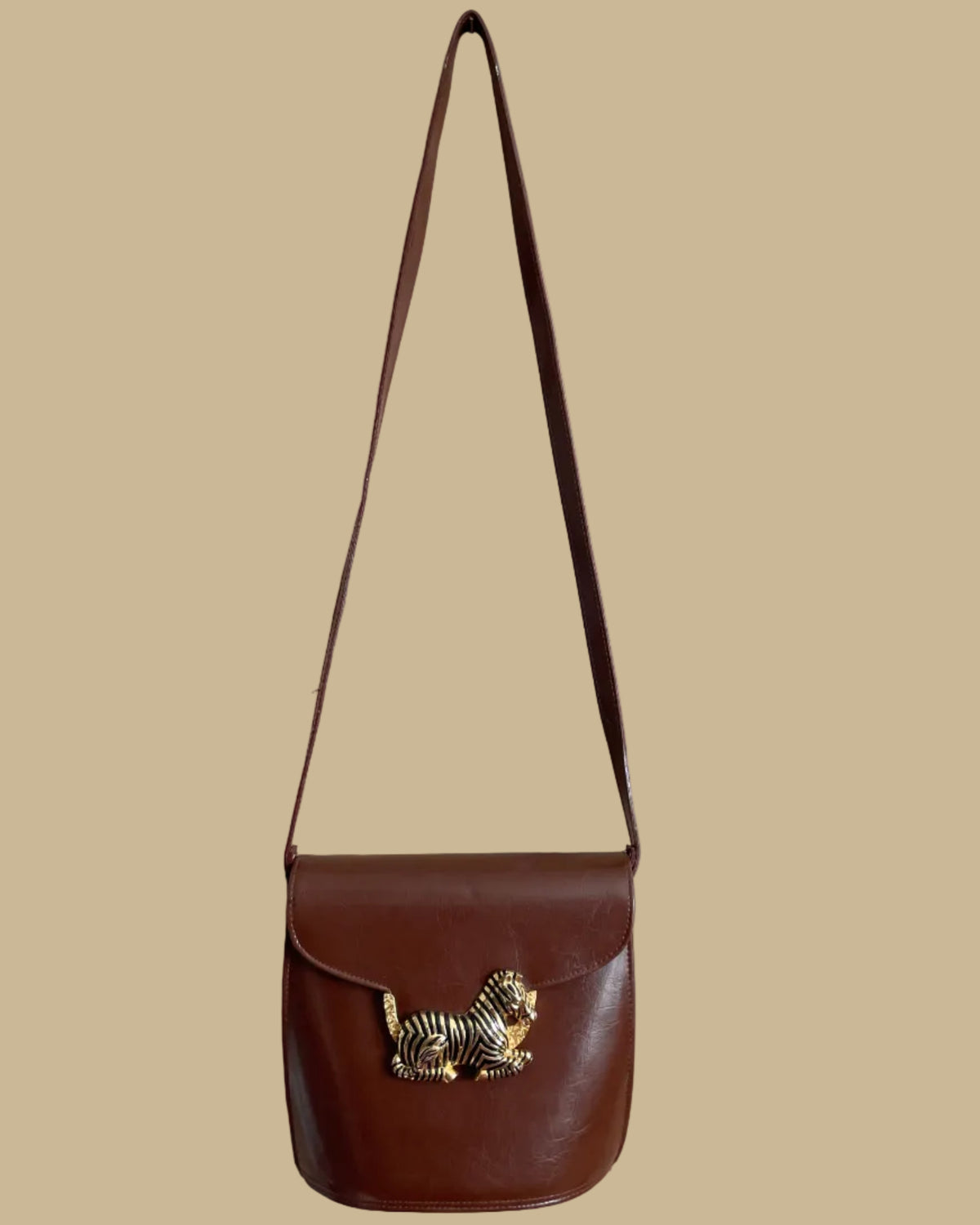 A vintage brown crossbody bag with a sculptural gold-tone and black enamel zebra clasp on the flap closure, shown against a kraft background