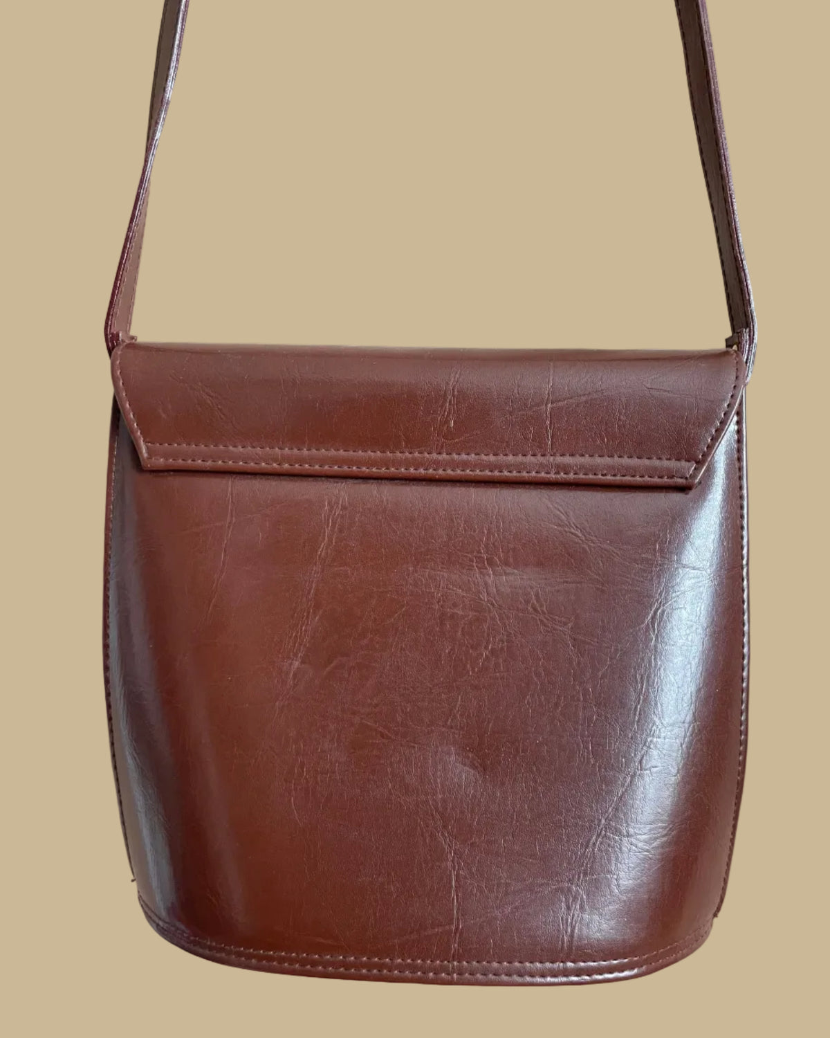 A vintage brown crossbody bag with a sculptural gold-tone and black enamel zebra clasp on the flap closure, shown against a kraft background