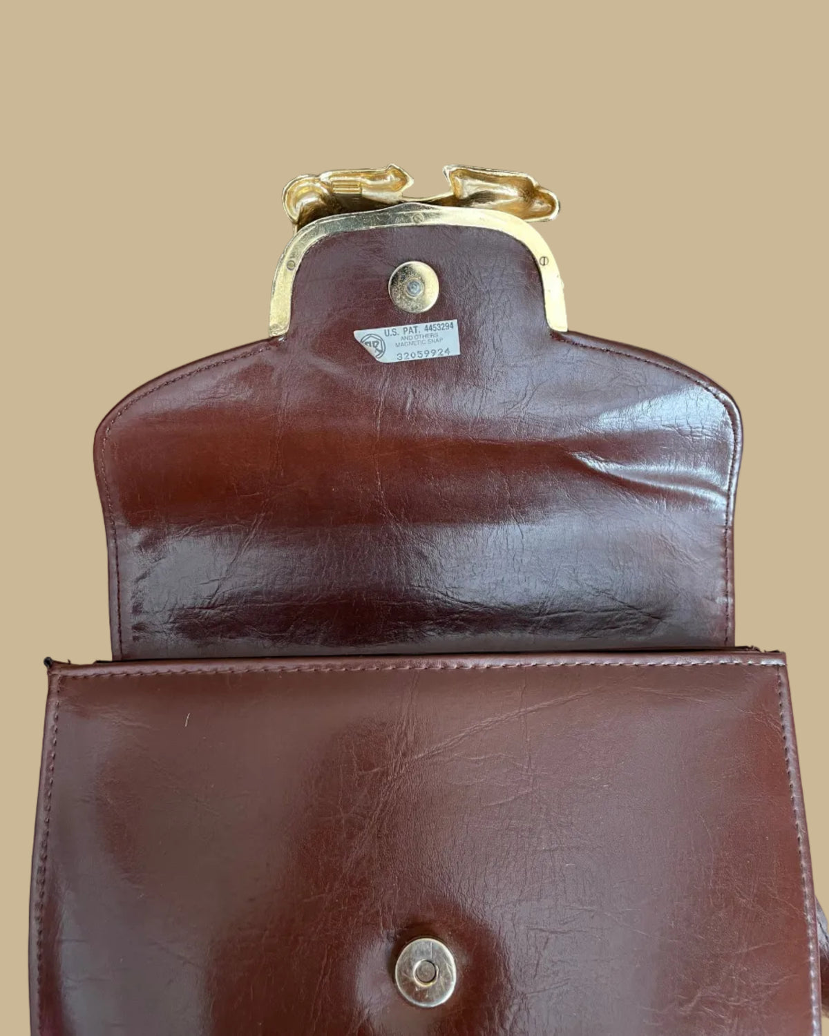 A vintage brown crossbody bag with a sculptural gold-tone and black enamel zebra clasp on the flap closure, shown against a kraft background