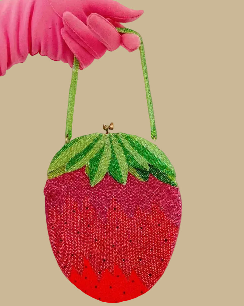 Strawberry-shaped handbag held by a pink gloved hand on a white background