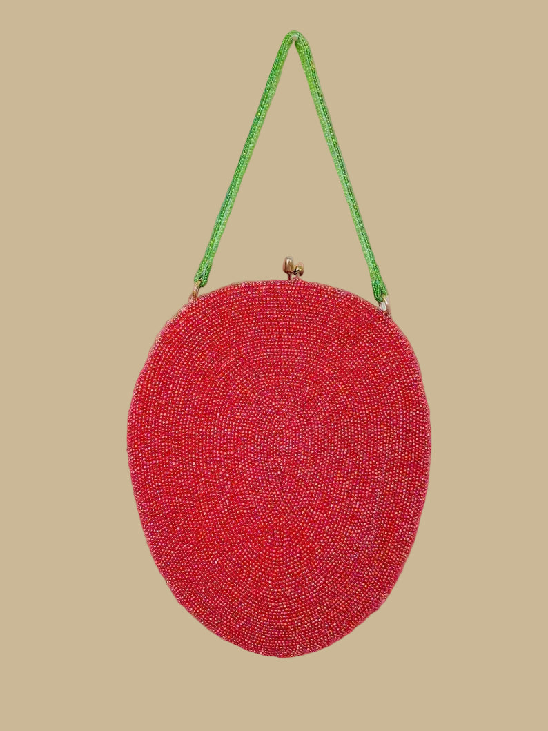 Red beaded handbag with a green strap on a beige background