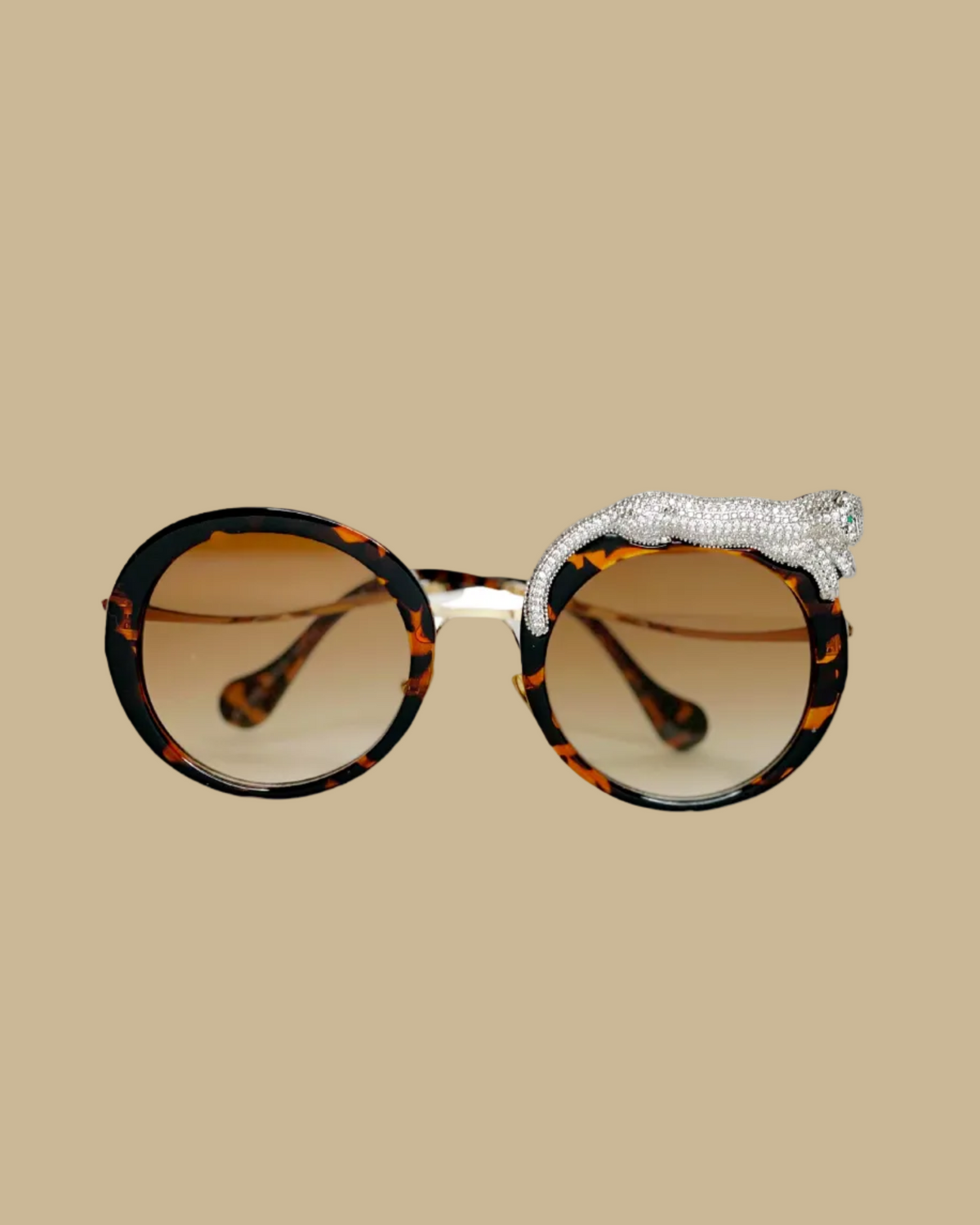 Retro-style sunglasses with a jeweled leopard figure lounging on one side, featuring emerald green jeweled eyes, in a tortoise brown colorway