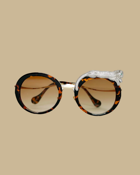 Retro-style sunglasses with a jeweled leopard figure lounging on one side, featuring emerald green jeweled eyes, in a tortoise brown colorway