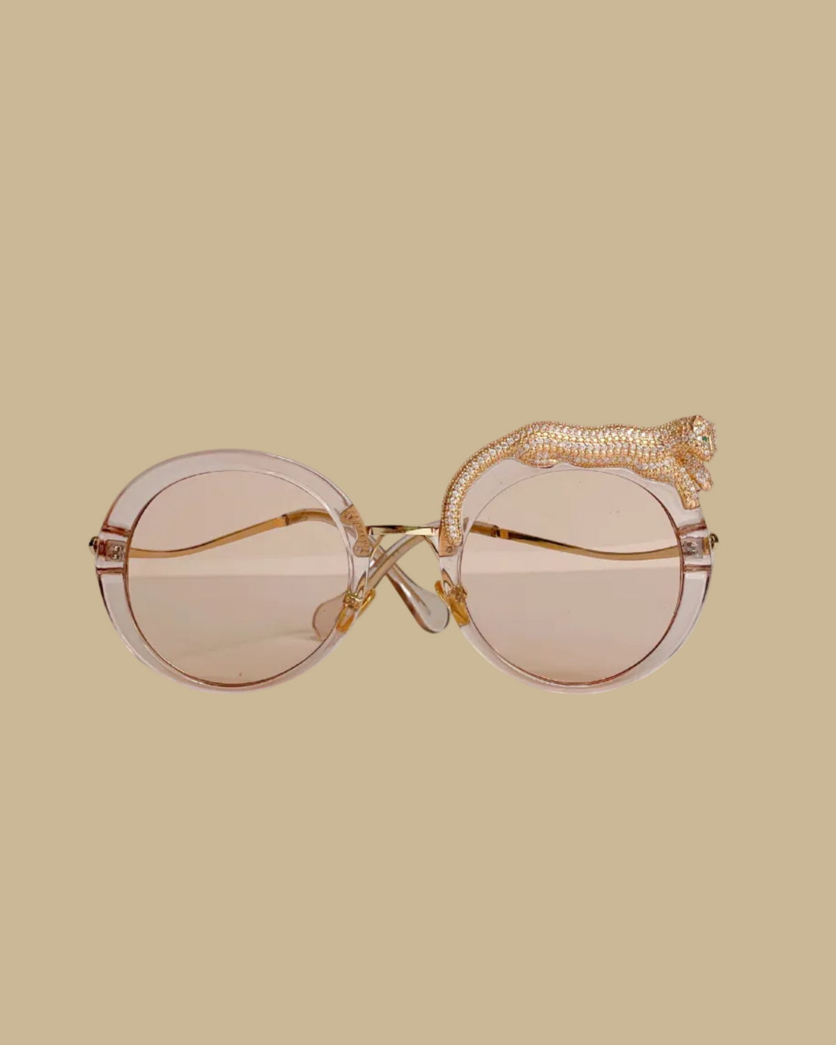 Retro-style sunglasses with a jeweled leopard figure lounging on one side, featuring emerald green jeweled eyes, in a rose champagne colorway